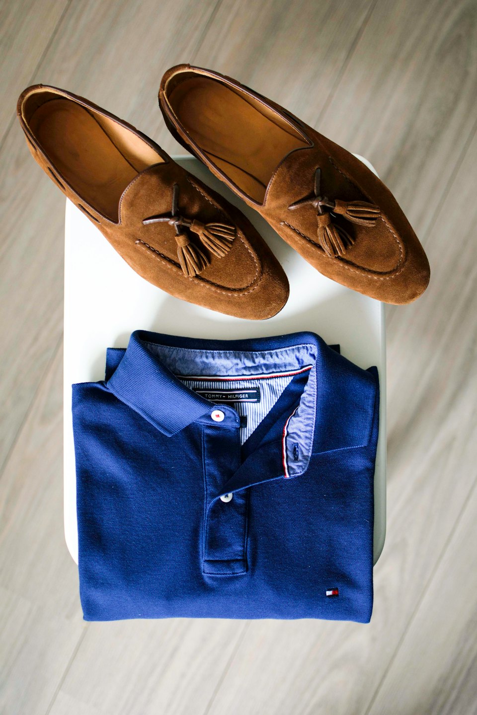 Navy polo shirt and brown loafers on a white surface.