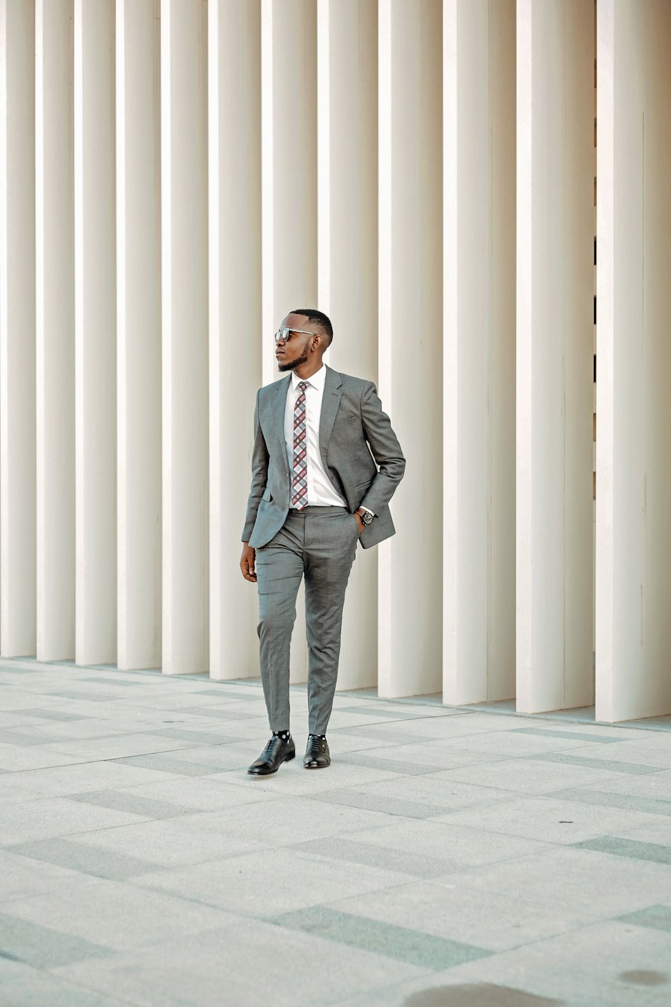 Young man in a grey suit walks outside near a modern building.